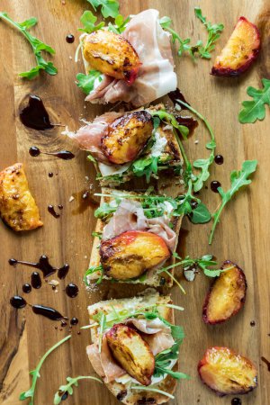 A peach and prosciutto baguette topped with arugula and balsamic glaze, cut into slices.