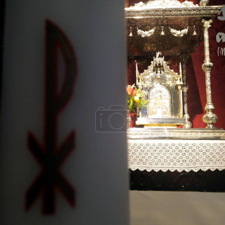 Foto de Illuminated silver tabernacle in the background in Catholic church in the foreground Christian symbol on the wall. - Imagen libre de derechos