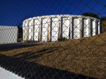 Foto de Water tank behind the metal fence on a blue sky that contrasts with the white tank. - Imagen libre de derechos