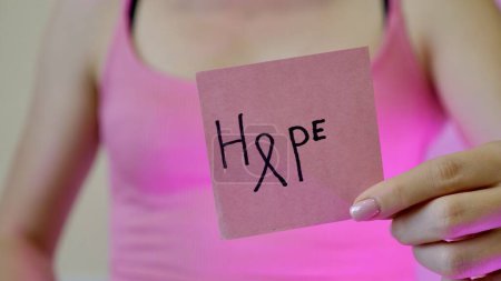 Foto de Mes de concienciación sobre el cáncer de mama. Inscripción esperanza en streaker rosa en mano femenina primer plano. - Imagen libre de derechos