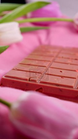 A bar of pink ruby chocolate with sublimated freeze-dried strawberries and almonds and spring tulip flowers . A dessert based on berries and nuts for International Womens Day, March 8, mothers day