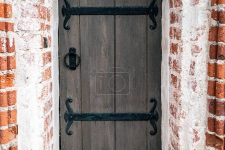 Téléchargez les photos : Porte en bois de style ancien avec charnières en fer décoratif et frappeur, sertie dans un mur de briques rouges. - en image libre de droit