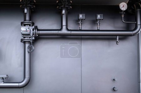 A close-up view of intricate industrial machinery featuring pipes, valves, and dials on a grey metal surface, highlighting mechanical engineering and technology.