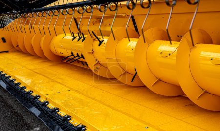 Detailed close-up of a yellow combine harvester's mechanisms with focus on the cutting blades and cylindrical parts, showcasing industrial agriculture machinery design and precision.