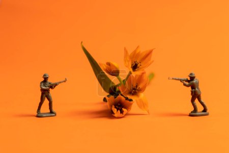 Zwei Miniatur-Spielzeugsoldaten und Sonnensternblume auf orangefarbenem Hintergrund