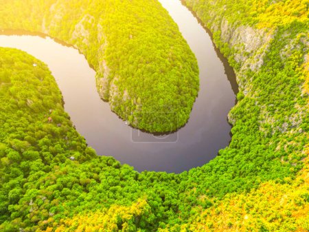 Eine Luftaufnahme eines ruhigen, gewundenen Flusses, der während der goldenen Stunde von üppigem Grün umgeben ist und die unberührte Schönheit der Natur zeigt.