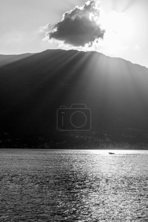 A tranquil scene capturing the serene beauty of a mountain lake at sunset. Sun rays pierce through a cloud, casting illuminating beams and sparkling reflections on the water surface. A lone boat