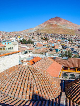 A view of the iconic Cerro Rico mountain looming over the terracotta rooftops of Potosi, Bolivia, on a clear day.