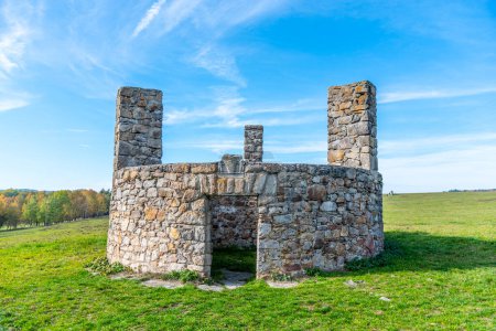 A stone structure standing in Horni Slavkov, which historically served as an execution ground, set against a clear blue sky and open field. Czechia