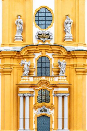 The ornate yellow and white baroque facade of Melk Abbey, adorned with sculptures and decorative windows, reflecting the grandeur of the historic monastery. Austria