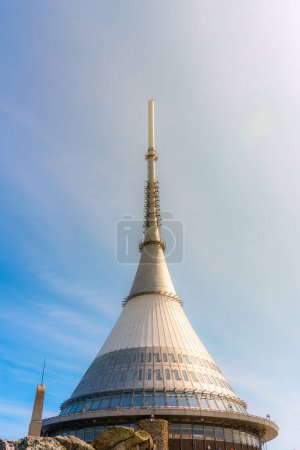 The Jested Tower, with its unique cone-shaped architecture, stands tall under a clear blue sky during sunny day. Liberec, Czechia
