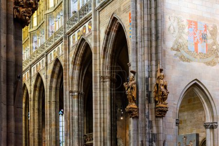 Die Gewölbedecken und gotischen Bögen des Innenraums des Veitsdoms werden durch heraldische Banner und aufwendige Skulpturen akzentuiert. Prager Burg, Prag, Tschechien