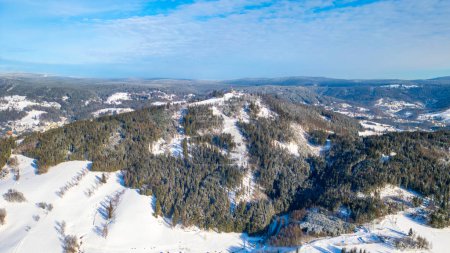 Blick aus der Vogelperspektive auf den schneebedeckten Tanvaldsky Spicak im Isergebirge mit kontrastierenden grünen Fichten. Tschechien