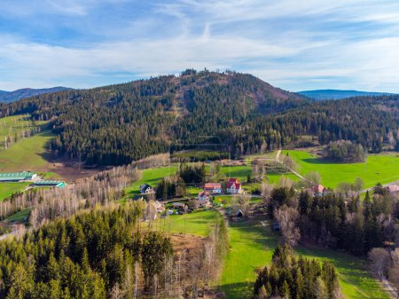 Eine ruhige Landschaft mit den üppigen Hängen des Tanvaldsky Spicak im Frühling, mit angrenzenden Wiesen und einer Ansammlung von Gebäuden an der Basis. Tanvald, Tschechien
