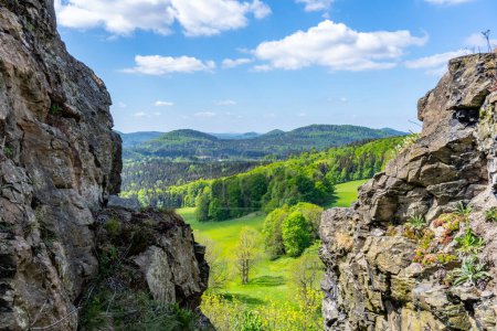 Une vue panoramique sur les montagnes Lusatiennes avec des falaises escarpées au premier plan et des forêts vertes denses s'étendant jusqu'à l'horizon sous un ciel nuageux. Tchéquie