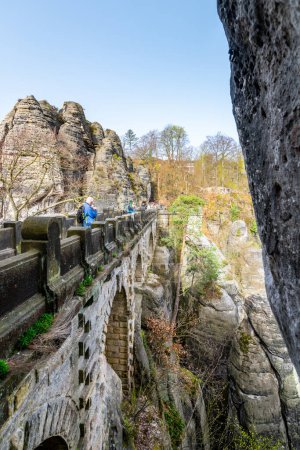 A senior traveler with a backpack and trekking poles walks on the Bastei Bridge amid sandstone formations in Saxon Switzerland National Park. Germany