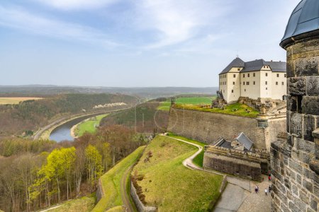 A view of the historic Konigstein Fortress in Saxony, with visitors on the ramparts and the Elbe River in the background. Garmany