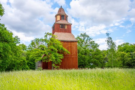 Die rustikale rote Holzfassade der Seglora-Kirche hebt sich an einem strahlenden Sommertag im Stockholmer Freilichtmuseum Skansen vom üppigen Grün ab. Schweden