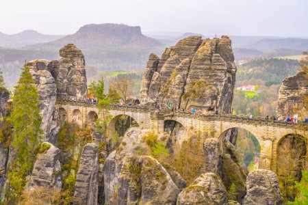 The Bastei Bridge stands tall among majestic sandstone rock formations with visitors enjoying the scenic view at sunset. Kurort Rathen, Saxon Switzerland, Germany