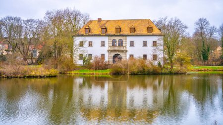 The historic Bad Muskau Chateau stands serene by a calm pond in Saxony, Germany, reflecting its grandeur in the water.
