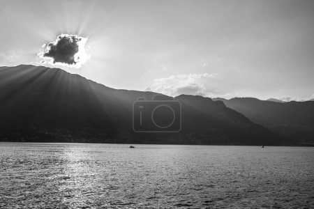 Eine ruhige Szene, die die heitere Schönheit eines Bergsees bei Sonnenuntergang einfängt. Sonnenstrahlen durchdringen eine Wolke und werfen leuchtende Strahlen und glitzernde Reflexe auf die Wasseroberfläche. Ein einsames Boot