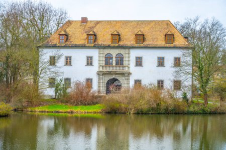 The historic Bad Muskau Chateau stands serene by a calm pond in Saxony, Germany, reflecting its grandeur in the water.