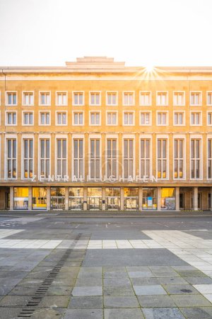 Sunlight flares above the historic Tempelhof Airport terminal in Berlin, casting a warm glow on its facade.