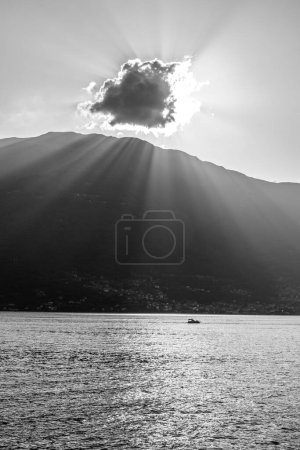 A tranquil scene capturing the serene beauty of a mountain lake at sunset. Sun rays pierce through a cloud, casting illuminating beams and sparkling reflections on the water surface. A lone boat