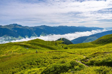 A hiker explores the lush trails of the Austrian Alps with a majestic mountainous backdrop and low-hanging clouds. Salzach Valley, Hohe Tauern, Austria