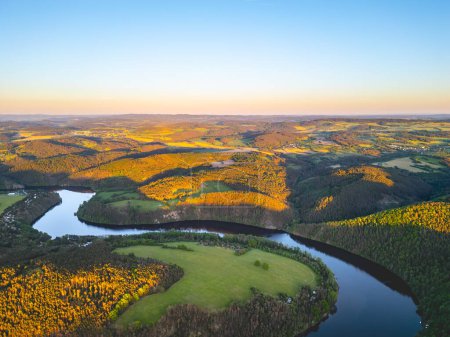 Vista aérea de la curva de herradura Solenice en el río Moldava en Chequia, mostrando el sinuoso río rodeado de exuberante vegetación y un pequeño pueblo durante una pintoresca puesta de sol.