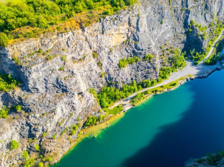 Aerial view of the abandoned Velka Amerika limestone quarry in Czechia with turquoise water surrounded by rocky cliffs and lush greenery on a sunny summer day.
