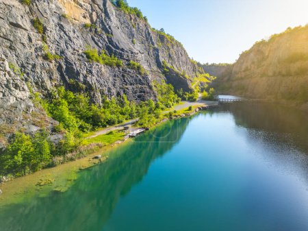 Sunlit limestone cliffs and tranquil water at Velka Amerika quarry in Czechia, captured at sunrise, showcasing the breathtaking natural scenery and geological formations.