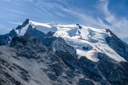 The towering Ortles Mountain stands grand under blue skies, its snowy caps and rugged terrain evincing the serene beauty of the Italian Alps.