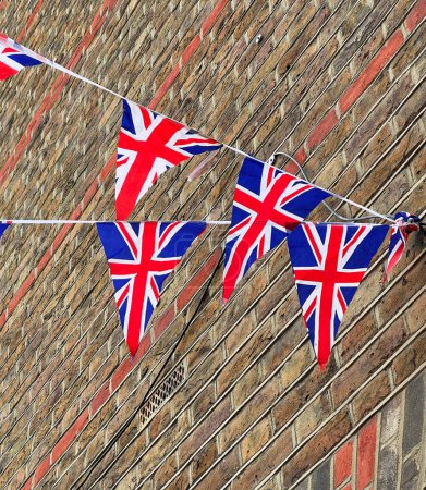 Photo for British Union Jack flags hanging at the street against brick wall, ready to national holiday celebration. Street party decorations in the UK city. Selective focus. - Royalty Free Image