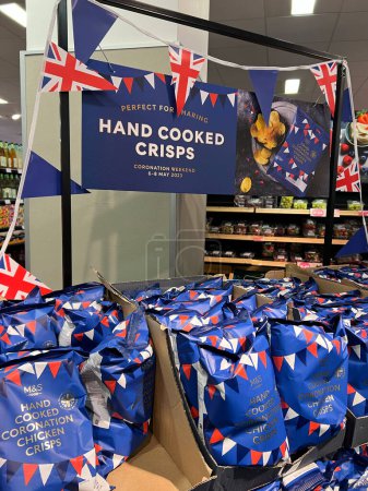 Photo for Hand cooked Coronation chiken crisps displayed at shelve of supermarket MarkSpencer in London - April, 2023. Merchandise commemorating the Coronation of King Charles III. - Royalty Free Image
