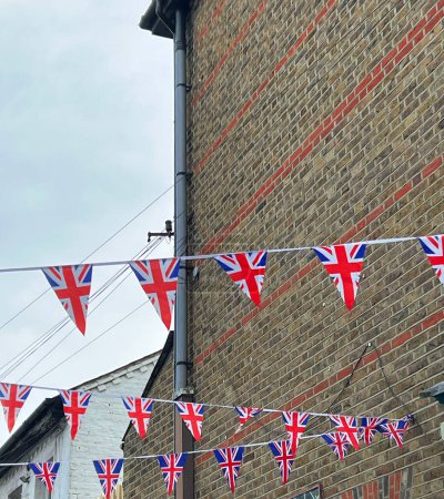 Photo for British Union Jack flags hanging at the street against brick wall, ready to national holiday celebration. Street party decorations in the UK city. Selective focus. - Royalty Free Image