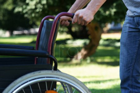 Erste Schritte auf eigene Faust - Mann schiebt leeren Rollstuhl Hochwertiges Foto
