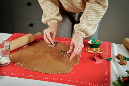 Foto de Mujer preparando galletas de jengibre en la cocina. Manos femeninas cortando masa de jengibre con cortador para hacer galletas para las vacaciones de invierno - Imagen libre de derechos