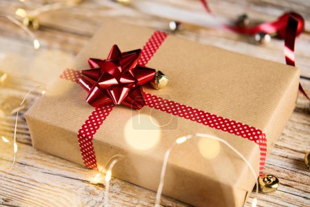 Foto de Vista superior de la caja de regalo festiva envolviendo en papel artesanal con cintas festivas y lazo. Regalo para las vacaciones de Navidad sobre fondo de madera con luces bokeh - Imagen libre de derechos