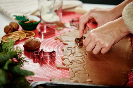 Foto de Las manos femeninas cortan las figuras de la masa de jengibre con el cortador. Cocinar galletas de jengibre para prepararse para las vacaciones de invierno. Hornear Navidad - Imagen libre de derechos