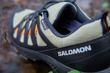 Photo for Salomon X Braze GTX hiking boots with Gore-Tex membrane in water puddle, surrounded by fallen leaves. Sturdy trekking shoes against backdrop of forest terrain. - Royalty Free Image