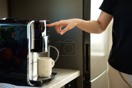 Foto de Mujer preparando una taza de café fresco con una moderna cafetera espresso. Pulsador de mano femenino en máquina de café - Imagen libre de derechos