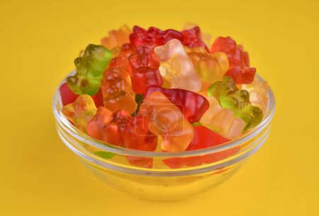 Photo for A lot of multi-colored jelly bears in a plate on a yellow background. Close-up. - Royalty Free Image