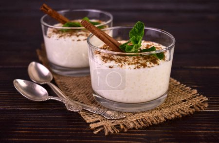 Rice pudding with cinnamon in glasses on a dark wooden background.