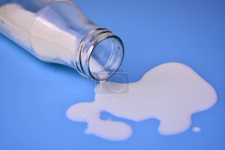 Botella de leche y derramada sobre un fondo azul. Primer plano.
