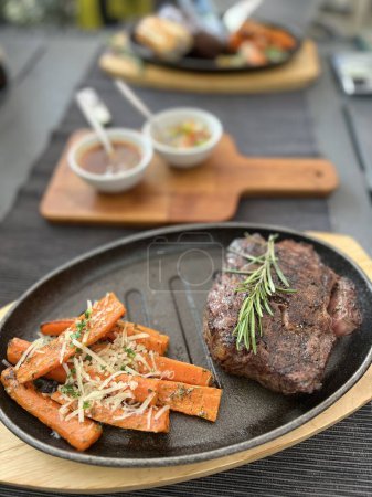 Grilled Steaks with spices rosemary and pepper on wooden board on black background.