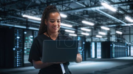 Photo for Portrait of Successful African American Female IT Specialist Using Laptop, Standing in Data Center. System Administrator Works on Web Services. Cloud Computing, Server Analytics, Cyber Security - Royalty Free Image