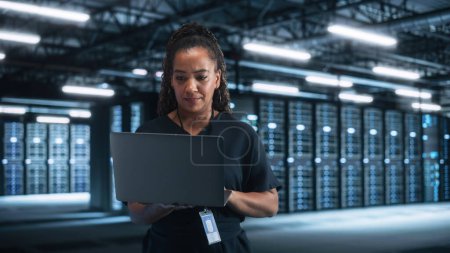 Photo for Successful Female IT Specialist Using Laptop Computer, while Standing at Big Warehouse Data Center. System Administrator working with Computing SAAS, Cloud Services. E-Business Digital Entrepreneur - Royalty Free Image
