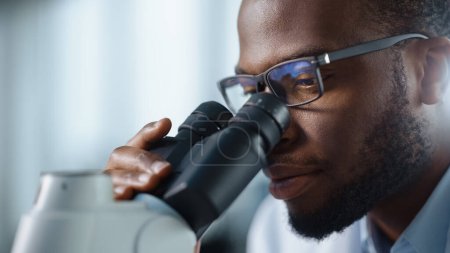 Photo for Macro Close Up Shot of a Handsome Black Male Scientist Wearing Glasses and Looking into the Microscope. Microbiologist Working on Molecule Samples in Modern Laboratory with Technological Equipment. - Royalty Free Image
