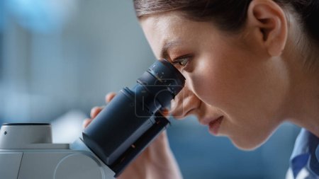 Foto de Macro Close-Up Shot of a Beautiful Female Scientist Looking into the Microscope. Microbióloga mujer que trabaja en muestras moleculares en laboratorio moderno con equipo tecnológico. - Imagen libre de derechos